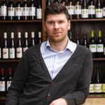 Matthias Hummel vor einem Weinregal mit verschiedenen Weinflaschen. Entdecken Sie die exquisite Auswahl an Lieblingsweinen mit Matthias Hummel!