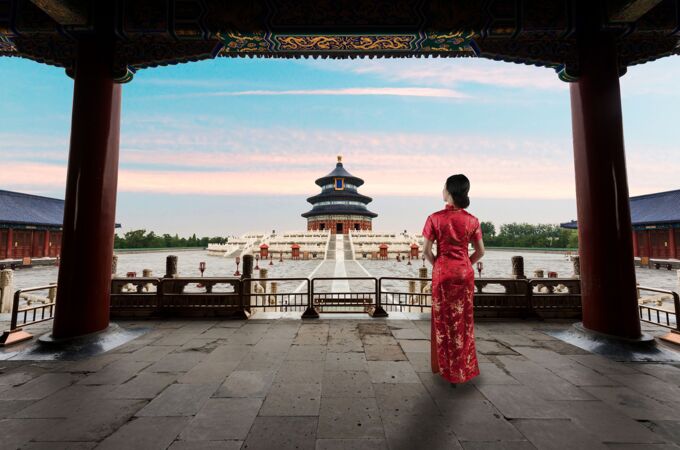 Eine Frau in traditioneller roter Seidenkleidung steht auf einer überdachten Terrasse und blickt auf den Himmelstempel in Peking, China.