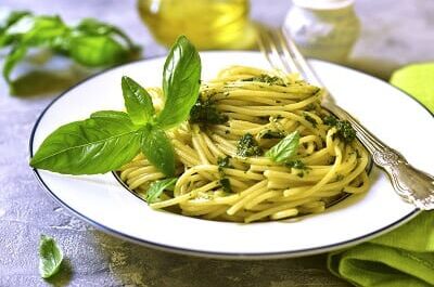 Ein Teller mit Spaghetti al Pesto, Basilikumblättern und einer Gabel, perfekt für ein mediterranes Weinerlebnis.