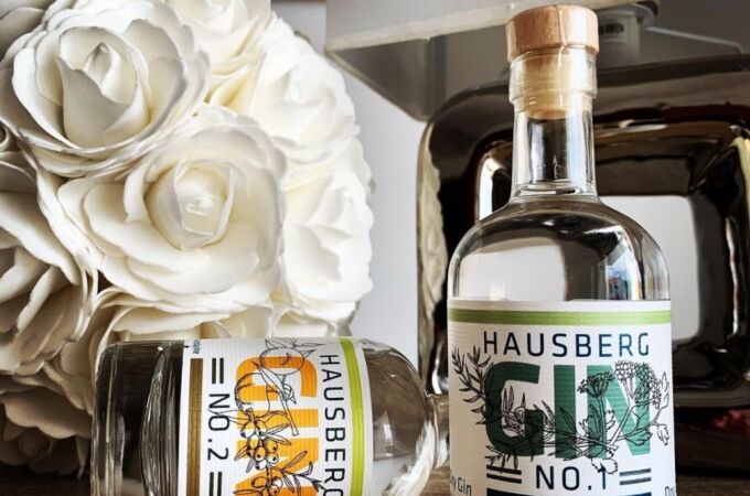 Zwei Hausberg Gin-Flaschen auf einem Holztisch, dekoriert mit weißen Blumen und einer Tischlampe.