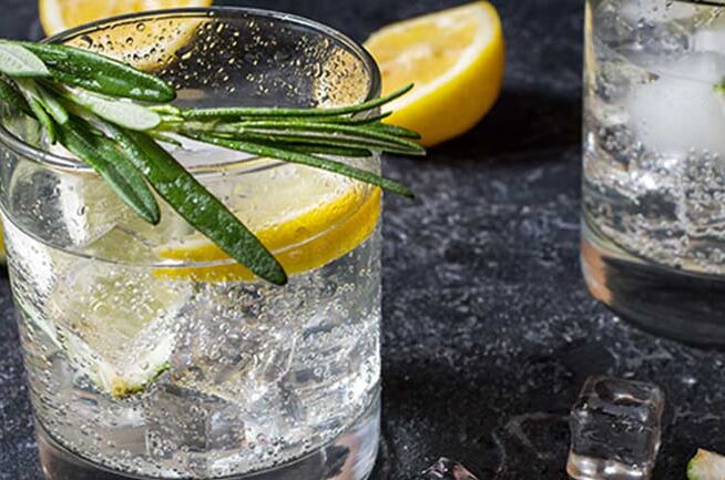 Zwei Gin-Cocktails in gläsernen Tumblern mit Eiswürfeln, frischen Zitronenscheiben und Rosmarinzweigen auf einem dunklen Untergrund.