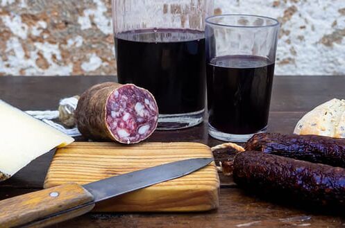 Holztisch mit Käse, Wurst, Brot und zwei Gläsern Rotwein. Typisches spanisches Wein- und Tapas-Arrangement. Genießen Sie den Geschmack Spaniens!