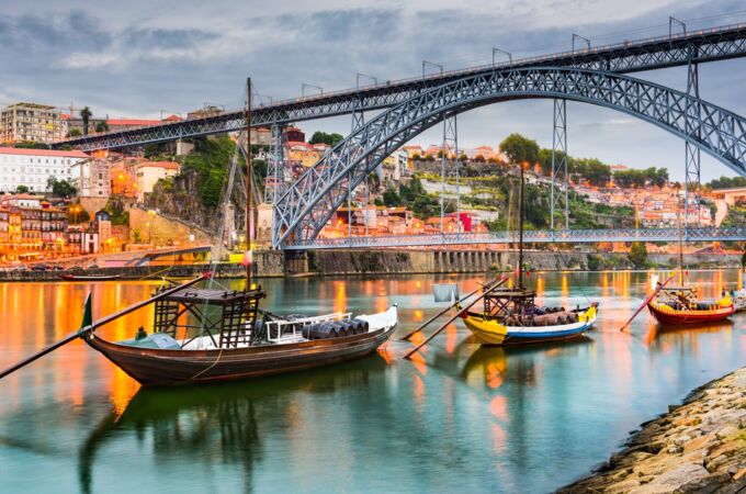 Boote auf dem Douro-Fluss in Porto, Portugal, bei Abenddämmerung mit beleuchteten Häusern und Brücke. Tauchen Sie in die magische Welt des Portweins ein!