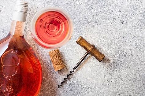 Flasche spanischer Roséwein, gefülltes Weinglas, Korken und Korkenzieher auf hellem Hintergrund. Genießen Sie spanischen Rosé!