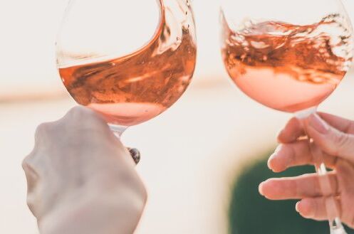 Zwei Personen stoßen mit Gläsern trockenen Roséweins im Freien an. Sonniger Hintergrund. Perfekt für Sommerabende!