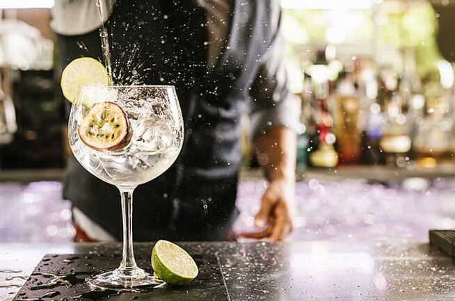 Ein Barkeeper gießt Gin über Eis in einem Ballonglas mit Limettenscheibe und Passionsfrucht in einer stilvollen Bar. Perfekt für Gin-Liebhaber!