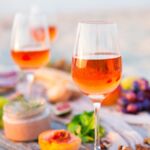 Orange Wine in schönen Weingläsern auf einem rustikalen Tisch mit Obst, Brot und Wurstwaren. Perfekte Sommerbegleitung!