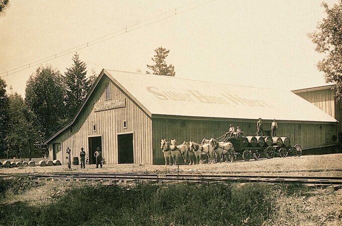 Historisches Foto der Sutter Home Winery mit Pferdekarren und Weinfässern, umgeben von Bäumen. Ein ikonischer Ort für echten Weingenuss!