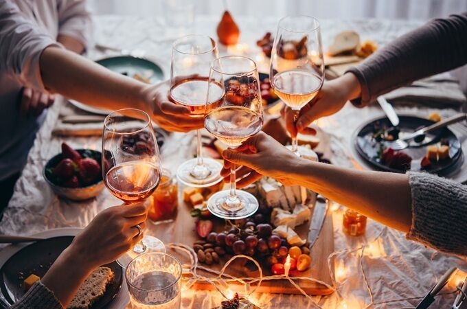Gruppe von Menschen stößt mit Gläsern Roséwein an, umgeben von Käse und Früchten auf einem gedeckten Tisch, ideal für gesellige Bio-Wein-Momente.