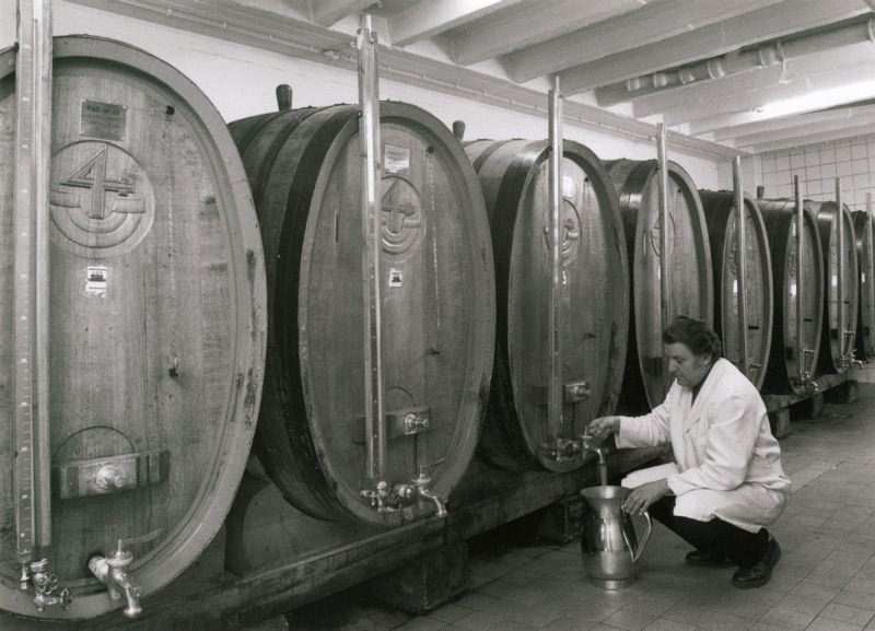 Ein Mitarbeiter zapft Wein aus einem großen Holzfass in einem historischen Weinlager. Diese Fässer dienten der Reifung hochwertiger Weine.