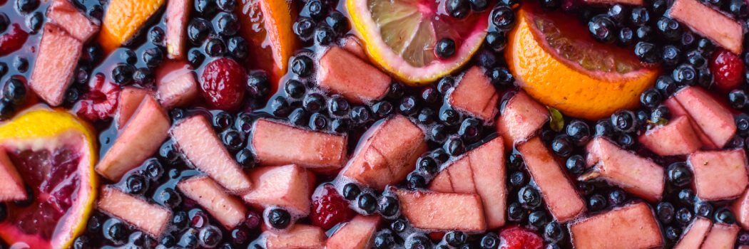 Bunte Sangria mit frischen Apfelstücken, Orangen- und Zitronenscheiben sowie schwarzen Johannisbeeren in einem Rotwein-Mix. Erfrischender Genuss!