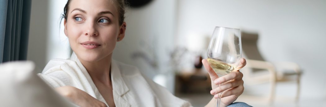 Junge Frau genießt Weißwein auf dem Sofa zu Hause. Perfekter Genuss-Moment für Weinliebhaber.